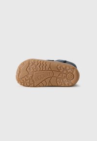 Donkerblauwe sneaker met een gestructureerde bovenkant, voorzien van een rubberen zool met een zigzagpatroon en reliëfbranding op de hak.