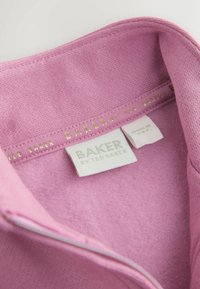 Cuello de sudadera rosa con una textura suave. Presenta un cierre con cremallera y etiquetas: "BAKER by Ted Baker" en dorado. La tela interior parece de felpa.