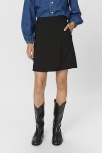 Jupe noire avec un design asymétrique et une texture lisse. Portée avec une chemise en denim bleu et des bottes en cuir noires.