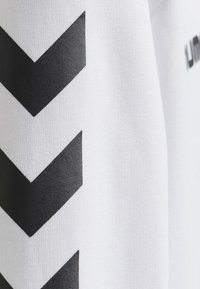 Il tessuto bianco presenta grandi motivi a zigzag neri. La texture è liscia con una leggera lucentezza, in contrasto con la grafica nera opaca.