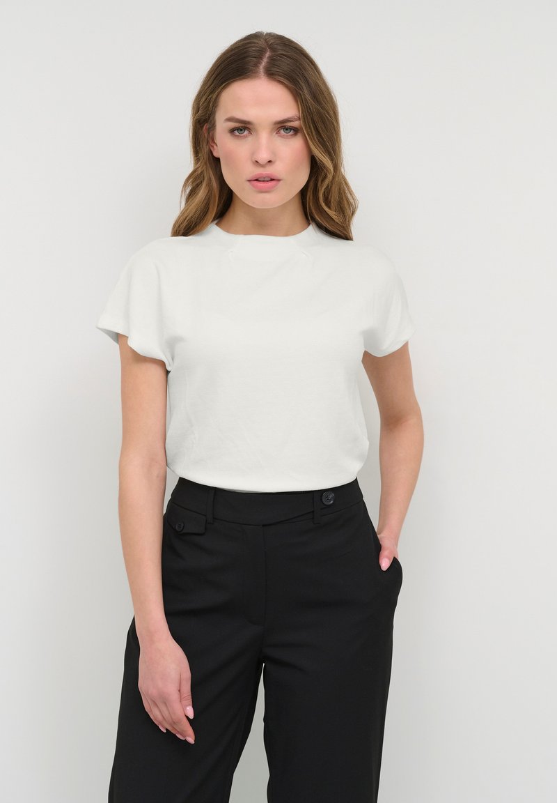 T-shirt bianco a maniche corte con scollatura rotonda, abbinato a pantaloni neri a vita alta con tasche frontali e dettaglio con bottone.
