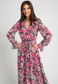Kwiatowa sukienka maxi z dekoltem w serek, długimi rękawami dzwonowymi i paskiem w talii. Materiał jest lekki i półprzezroczysty w odcieniach różu i zieleni.