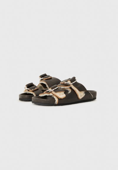 Black slide sandals with cowhide accents, featuring two adjustable straps and silver-tone hardware. Textured sole for grip.