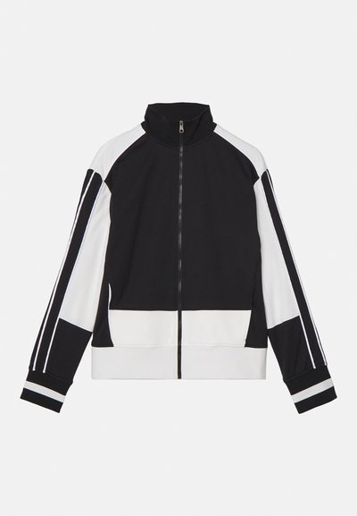 Black and white zip-up jacket with high collar, featuring contrasting shoulder stripes and banded cuffs. Soft fabric with a minimal design.