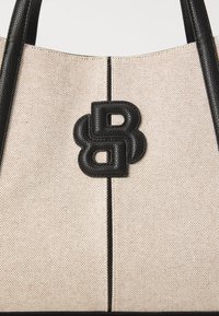 Beige strukturert totebag med svarte lærdetaljer og en karakteristisk svart logo. Har doble svarte håndtak og sømdetaljer.
