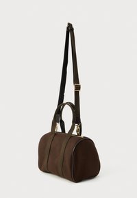 Καφέ δομημένη τσάντα duffel με διπλά κοντά χερούλια και ρυθμιζόμενο μακρύ λουρί ώμου κρεμασμένη σε λευκό φόντο.