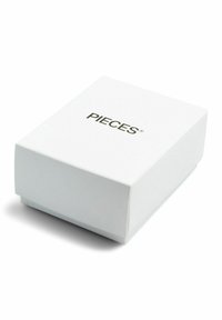 Boîte rectangulaire blanche à texture lisse, avec un logo imprimé "PIECES" en noir sur la surface supérieure. Design fermé et simple.