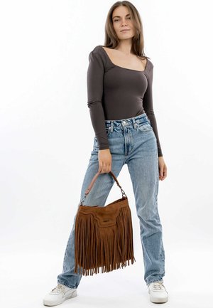 Braune Wildleder-Handtasche mit Fransen, hellbraunen Lederakzenten und einem kurzen Griff, kombiniert mit einem eng anliegenden Langarmoberteil und hellblauen Jeans.