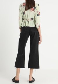 Blomstrede peplum bluse i lysegrøn, med farver som pink og sort. Sammen med sorte, cropped wide-leg jeans.