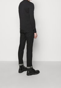 Black long-sleeve shirt, dark jeans with rolled cuffs, and black ankle boots. The outfit features a simple design and fitted style.