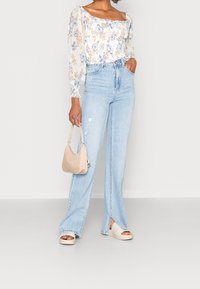 Blusa floreale a maniche lunghe, jeans a vita alta azzurri chiari con dettagli strappati, borsa a spalla beige e sandali platform bianco sporco.
