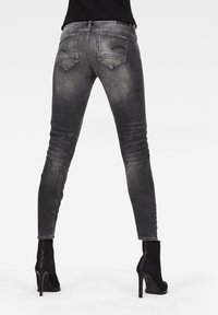 Jeans de mezclilla negra ajustada con un lavado desgastado, cintura alta y dos bolsillos traseros. Combinados con botines negros de tacón de aguja.
