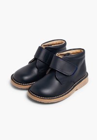 Botas de tobillo de piel en color navy con una correa de velcro, punta redonda y suela de goma beige que presenta costuras visibles a lo largo del borde.