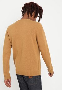 Beżowy sweter dzianinowy z długimi rękawami, prążkowanymi mankietami i dolną krawędzią, okrągłym dekoltem, charakteryzujący się teksturowanym wykończeniem oraz małą etykietą marki z tyłu.