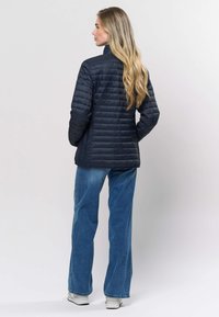 Tamsiai mėlyna pūkinė striukė su vertikaliais siūlais. Savo aukštu apykakle, derinama su šviesiai mėlynais platėjančiais džinsais ir baltais sportbačiais.