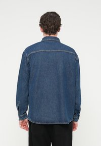 Σκούρο μπλε τζιν πουκάμισο με κλασικό γιακά, μακριά μανίκια και μανσέτες με κουμπιά, με ίσια γραμμή και λεπτομέρεια ραφής στο πίσω μέρος.