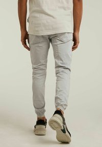Pantalon jogger gris clair fuselé avec poignets élastiques, conçu avec des poches arrière et une texture lisse, associé à des baskets noires et grises.