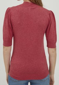 Röd kortärmad tröja med ribbad rundhals och puffärmsdesign. Mjuk textur med en jämn yta. I kombination med blå jeans.