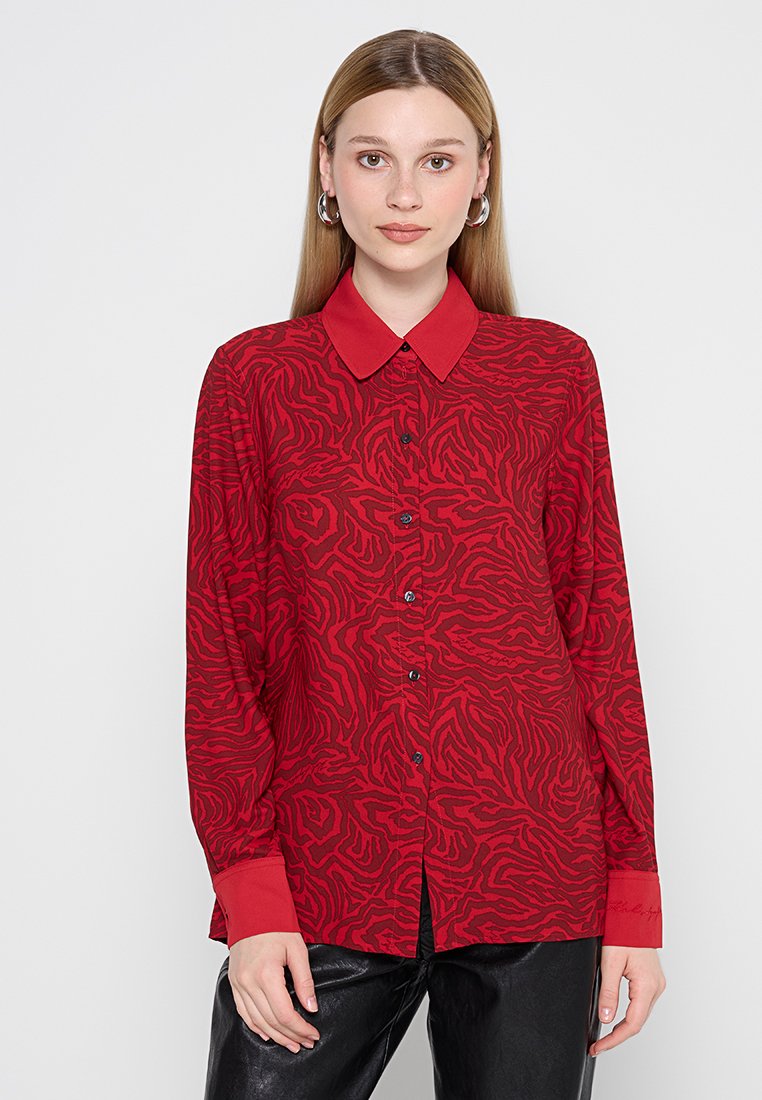 Chemise rouge à manches longues avec un motif zèbre texturé, un col et des boutons noirs, avec des poignets rouges contrastants et des détails de couture.