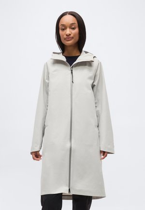 Moterys dėvi šviesiai pilką ilgą lietpaltį su priekyje esančiu užtrauktuku ir gobtuvu, stovinti prieš paprastą baltą foną.