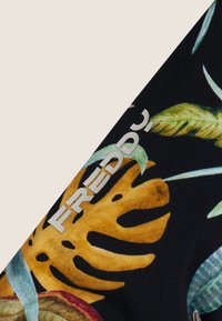 Musta kangas, jossa on vihreä- ja oranssivärinen trooppisten lehtien kuvio, ja harmaa "FREDDY"-logo reunassa.