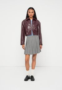 Jachetă scurtă bordo cu finisaj lucios, combinată cu un top albastru deschis și o fustă plisată în carouri alb-negru, purtată cu pantofi negri și șosete albe.