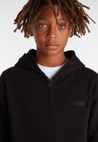 Svart zip-upp hoodie med en texturerad tyg, med en framdragkedja och en sydd Vans-logotyp på bröstet. Design med huva.