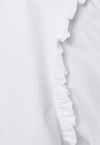 Tecido branco com uma textura suave apresenta uma borda franzida de um lado, proporcionando um detalhe de design suave e dimensional.