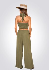 Conjunto de dos piezas en verde oliva que incluye un top halter fruncido con lazo en la espalda y pantalones de pierna ancha holgados, confeccionados en una tela ligera.