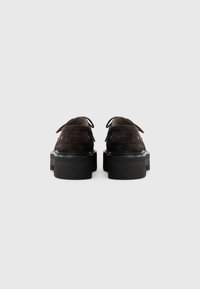 Scarpe in suede marrone scuro con punta arrotondata, due cinturini decorativi e una robusta suola nera a piattaforma. La vista posteriore mostra dettagli di cucitura.
