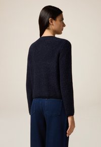 Maglione lavorato a maglia di colore blu navy con finitura morbida e strutturata, collo rotondo e maniche lunghe, abbinato a jeans a gamba larga di colore blu scuro.