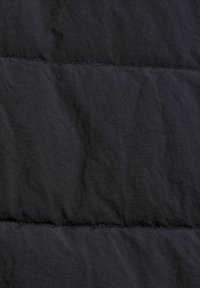 Svart pufferjacka i tyg som visar kviltade sektioner med en något skrynklig textur. Sömmen är synlig och indikerar en isoleringsdesign.