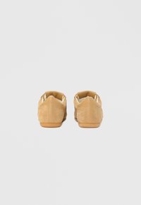 Chaussures en daim beige à profil bas et bout arrondi. Elles présentent une semelle en caoutchouc lisse et des détails de couture discrets sur les côtés et à l'arrière.