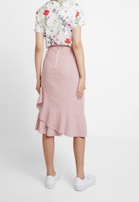 Bílé květinové tričko s krátkým rukávem, spárované s červenou a bílou pruhovanou midi sukni s volánovým lemem a bílými teniskami.