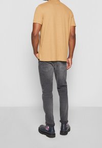 Chemise à manches courtes beige en coton, associée à un jean slim gris foncé et des bottes sombres avec des accents colorés sur les talons.