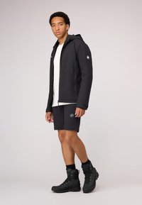 Svart vattentät jacka med huva, bärs över en vit skjorta. Matchas med svarta shorts och robusta svarta vandringskängor. Enkel design.