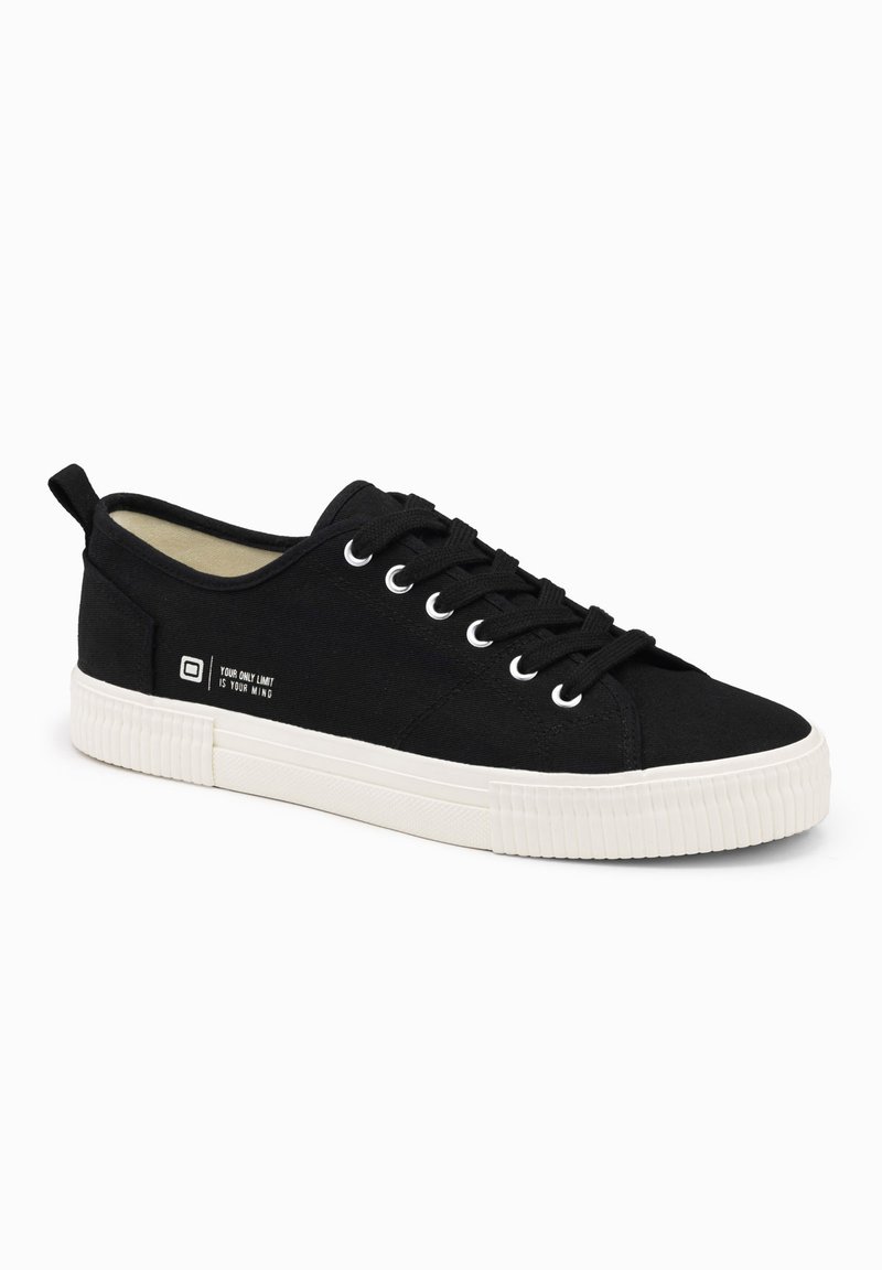 Sneakers neri in tela con suola in gomma bianca, punta rotonda, sei asole e un dettaglio stampato sul lato. Parte superiore testurizzata con design minimal.