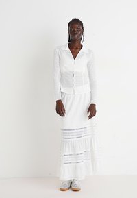 White button-up shirt with mesh panels, paired with a long, tiered white skirt featuring lace accents. Grey sneakers complete the outfit.
