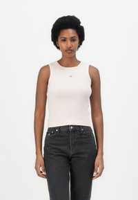 Canotta a coste rosa chiaro con scollatura rotonda, caratterizzata da un piccolo logo sopra il petto. Abbinata a jeans grigio scuro.