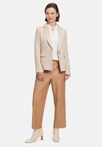 Blazer beige chiaro strutturato con un solo bottone, abbinato a pantaloni a gamba larga in finta pelle marrone chiaro e stivaletti crema.