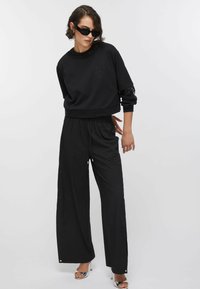 Sweat-shirt noir à manches courtes, présentant un logo discret. Associé à un pantalon noir à jambes larges, tous deux avec une texture lisse et une coupe décontractée.