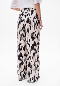 Pantalons larges en tissu léger, avec un imprimé léopard noir et rose sur fond crème. Détail de taille élastique.