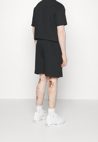 Black cotton t-shirt and shorts worn with white sneakers. Shorts have an elastic waistband and slight side slits; visible stains on legs.