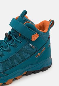 Turquoise wandelschoen met oranje accenten, voorzien van een klittenbandsluiting, een gestructureerd mesh bovenwerk en een robuuste zwarte en oranje rubberen zool.