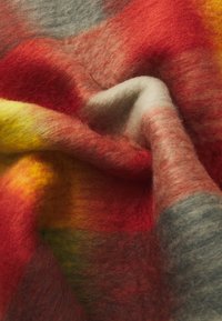 Manta de lana con una mezcla de colores cálidos: rojo, amarillo y gris. Tejido suave y texturizado con patrones de degradado sutiles y bordes suaves.