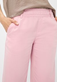 Lichtroze, elastische taillebroek met zijzakken en een gladde textuur. De zoom is recht met zichtbare stikseldetails.