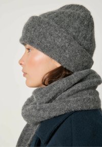 Grå strikket hue og tørklæde lavet af blødt, tekstureret stof, der viser en rullet manchet på huen, lagdelt omkring halsen.