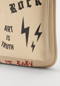 Beige tekstureret taske hjørne med sorte lyn, teksten "ROCK" og "KUNST ER SANDHED," samt rød håndskrift delvist synlig i bunden.