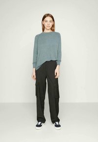 Heller blauer, lockerer Pullover mit langen Ärmeln, kombiniert mit schwarzen Cargo-Hosen mit Streifen und Seitentaschen, getragen mit marineblauen Sneakern.
