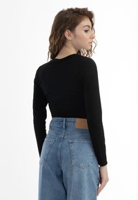 Maglietta crop a maniche lunghe nera a coste abbinata a jeans in denim blu chiaro a vita alta con una patch in pelle marrone sul retro.
